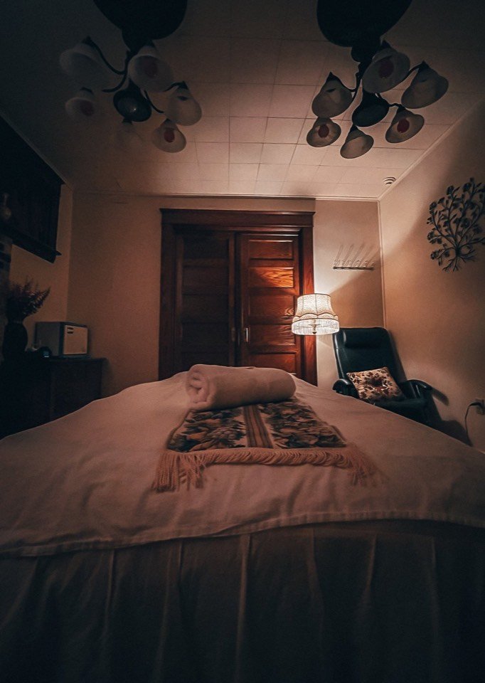A treatment room lit by a warm lamp with a made-up massage table